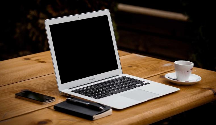 A laptop on a wooden desk next to a coffee cup